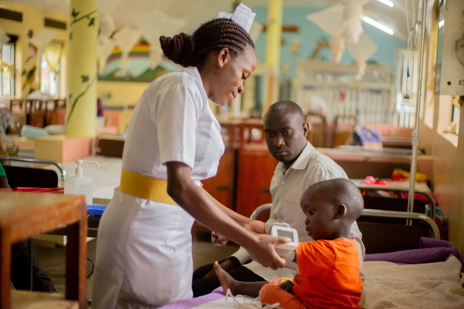 Nurse checking on a young boy sitting with his father in a paediatric ward
